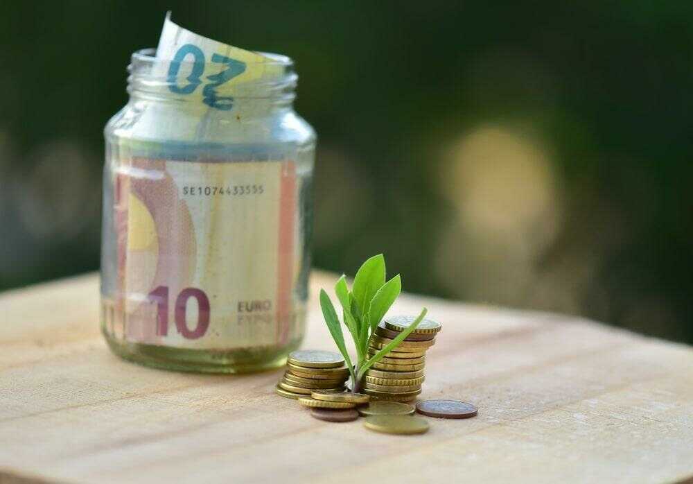 Un pot en verre servant de tire-lire contenant de billets, à côté de pièces de monnaie